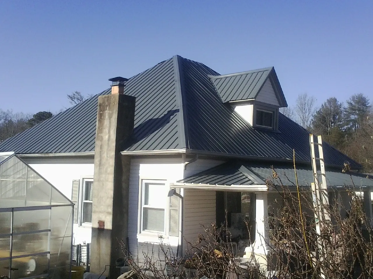 Dark blue standing seam metal roof on a white farmhouse with dormer — Slate & Tile Roof Repair by Roofing Brothers in Woody Creek