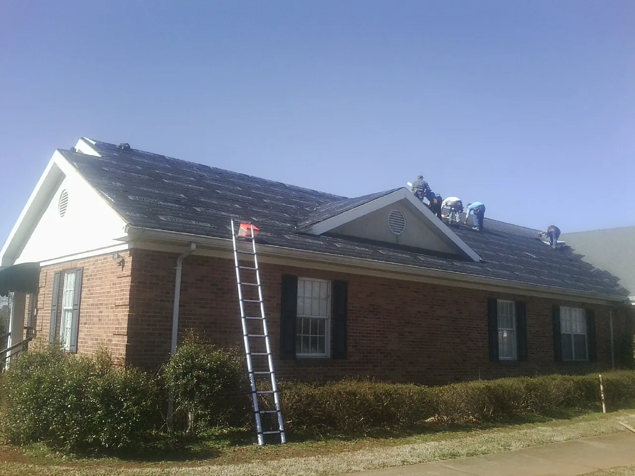 Crew tearing shingles off a brick ranch roof with a ladder set — Metal Roof Repair work by our crew in Woody Creek
