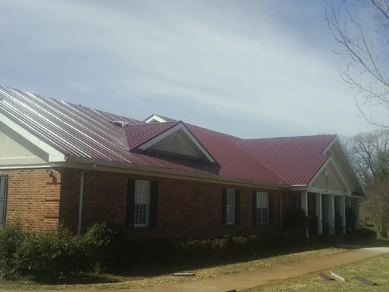 Red metal roof with gabled entries on a long brick building, from a Hail Damage Roof Repair job in Woody Creek