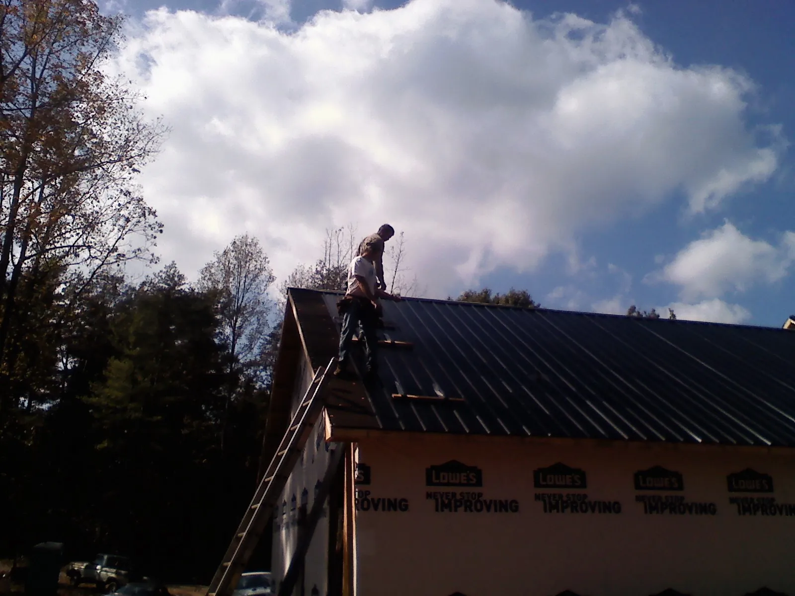 Roofer fastening dark metal panels high against a cloudy sky in Woody Creek