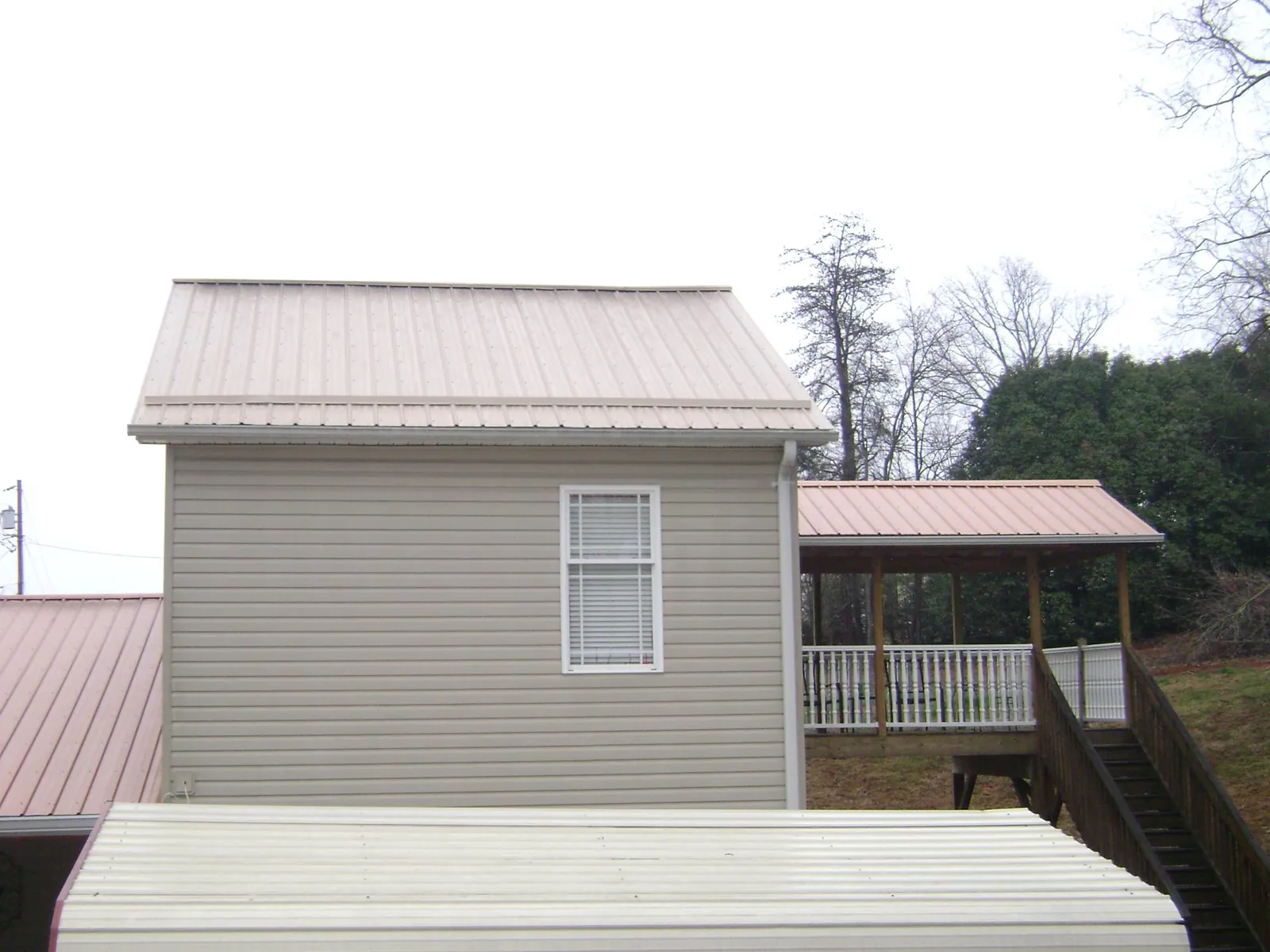 Tan metal roofs on a two story addition and attached porch, from a Roof Replacement job in Woody Creek